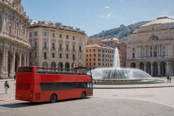 A plain open-top double-decker sightseeing bus without markings stopped beside a wide oval fountain square lined with grand palaces, Piazza De Ferrari