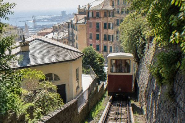 A small old cable railway car climbing a steep cutting between stone walls with a few passengers seen through the windows from behind, Zecca-Righi Funicular