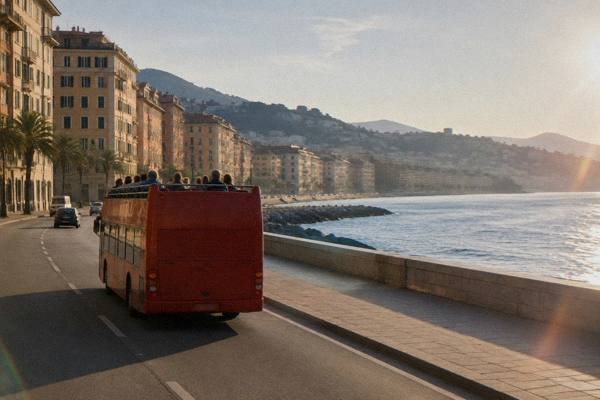 A plain open-top sightseeing bus without markings passing along a seafront road beside a low sea wall and the open sea, Corso Italia