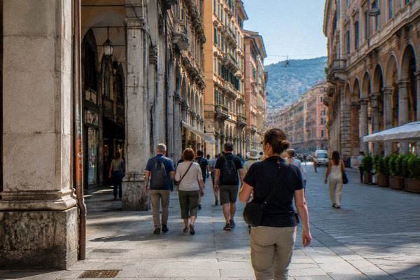 A small walking group crossing a broad arcaded boulevard behind a guide, tall stone buildings with ornate cornices on both sides, Via XX Settembre
