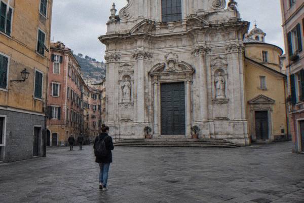 A lone visitor with earphones in, walking slowly across a small paved square toward a Baroque church front, Chiesa del Gesù