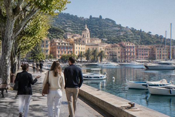 A private guide and a couple seen from behind strolling a waterfront promenade beside a harbour of moored boats and pastel buildings, Santa Margherita Ligure