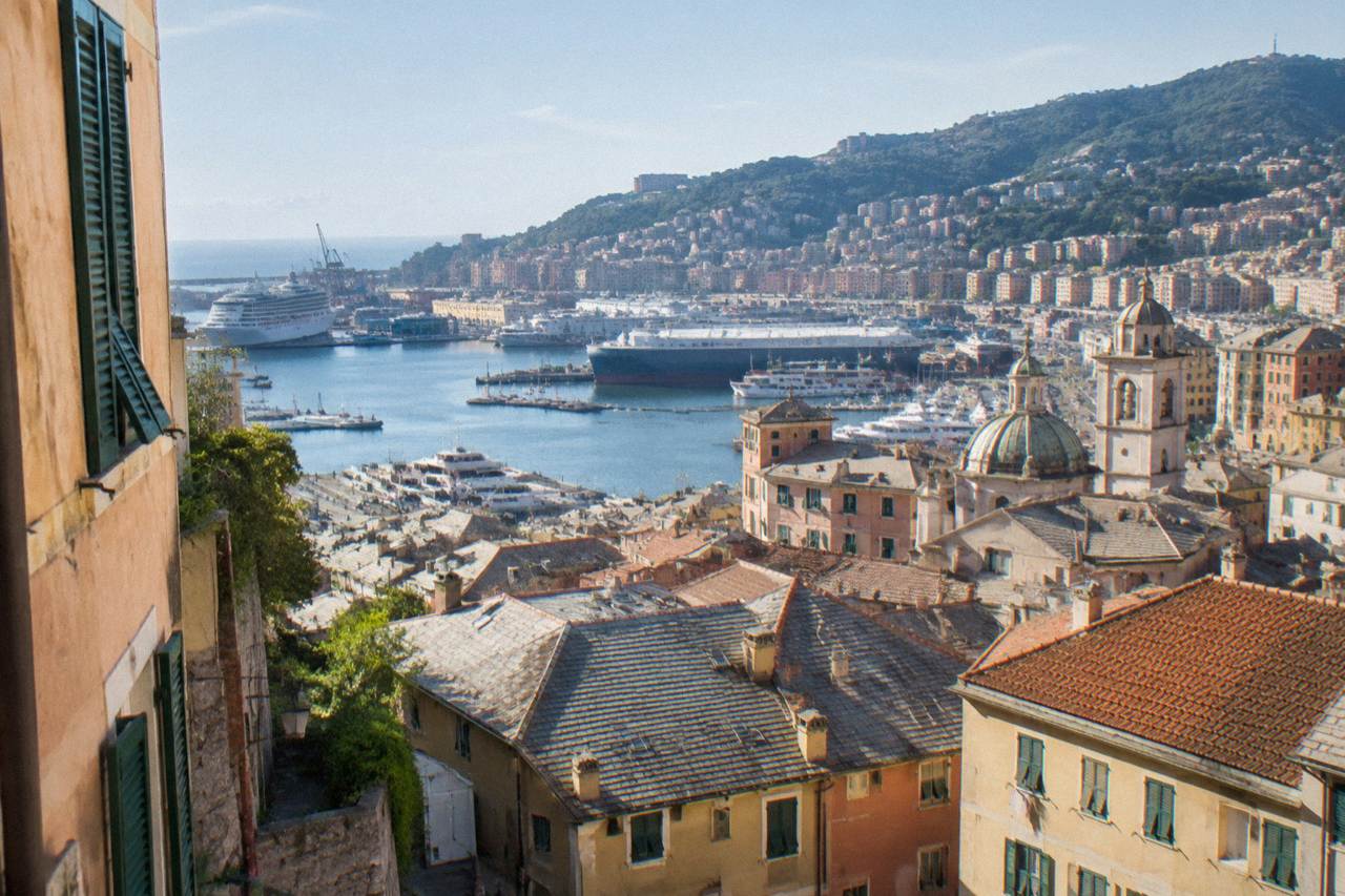 The harbour of Genoa with ships moored along the piers and hills rising behind the city