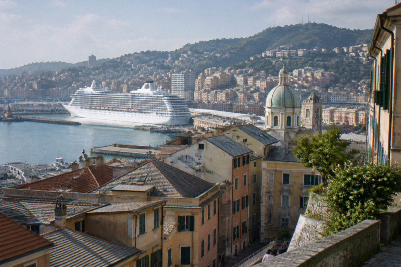 Cruise ship docked at a terminal in Genoa with the city and hills rising behind the harbour