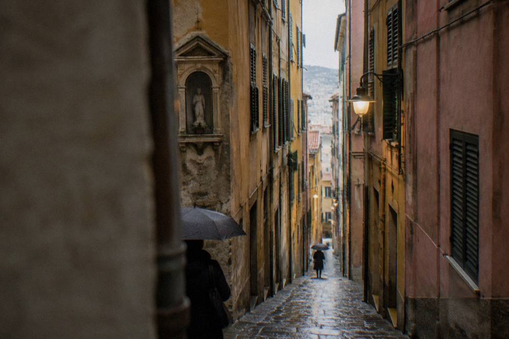 A narrow cobbled lane in the caruggi of Genoa's old town with tall coloured buildings on both sides