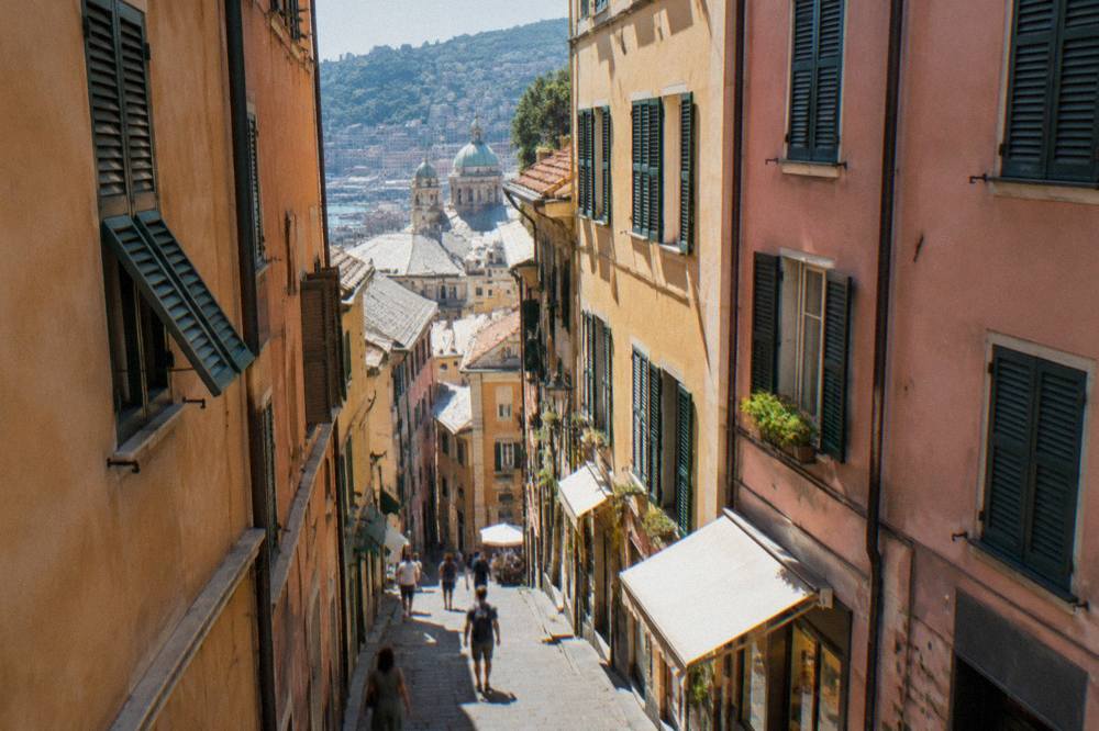 A narrow alley in the medieval old town of Genoa with tall painted buildings and shopfronts