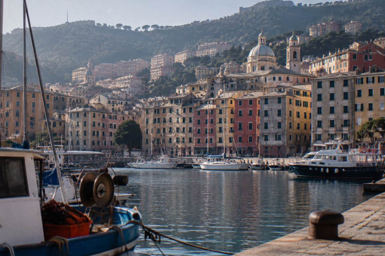 Colourful apartment buildings rising above a small Mediterranean harbour with wooded hills behind