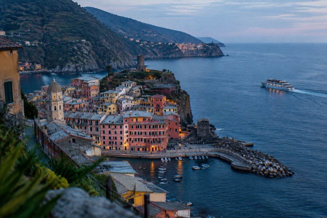 A passenger ferry cruising along a rocky Ligurian coastline with colourful cliffside villages in the distance