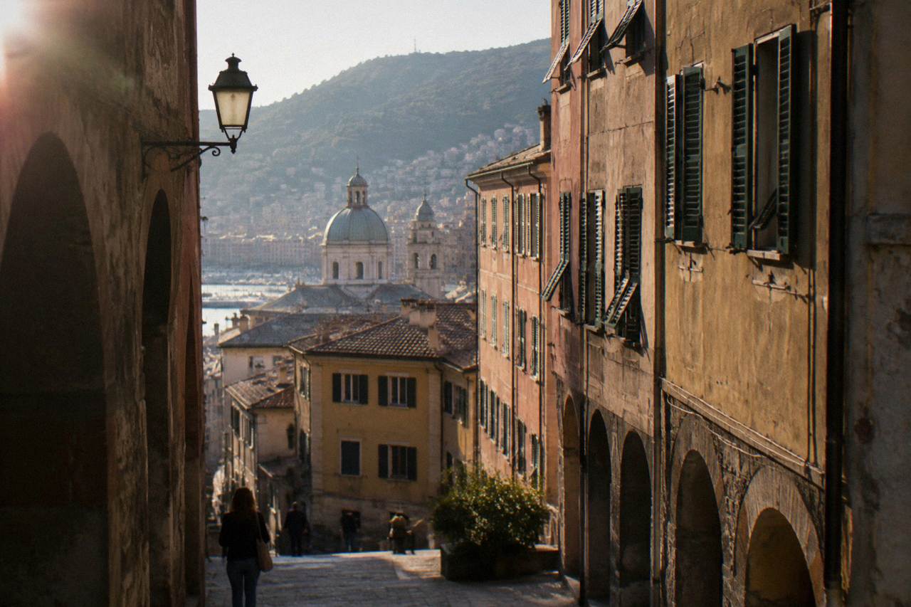 A narrow lane in the old town of Genoa with stone arches and shuttered buildings