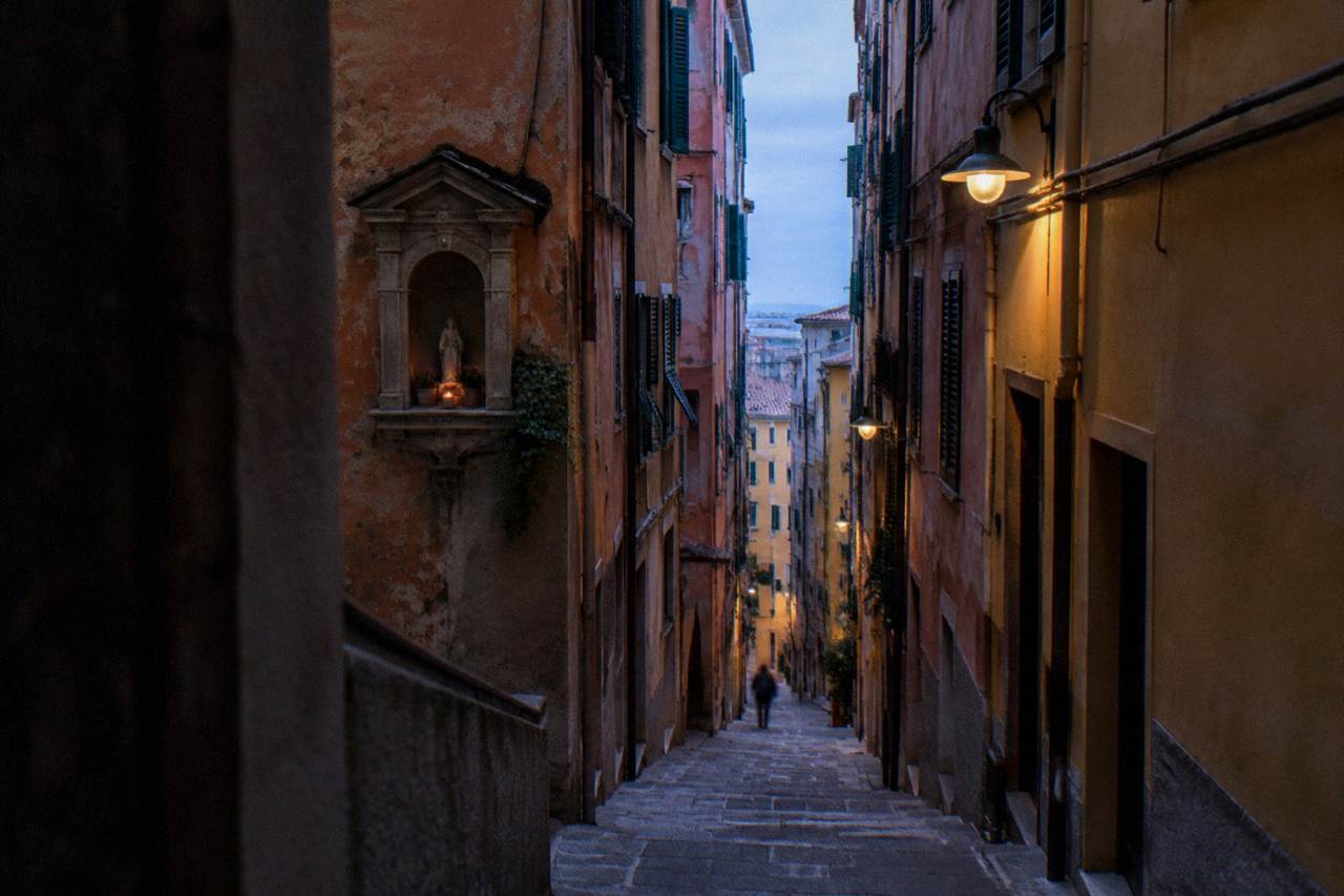 Narrow caruggi alley in the old town of Genoa with tall coloured buildings on both sides