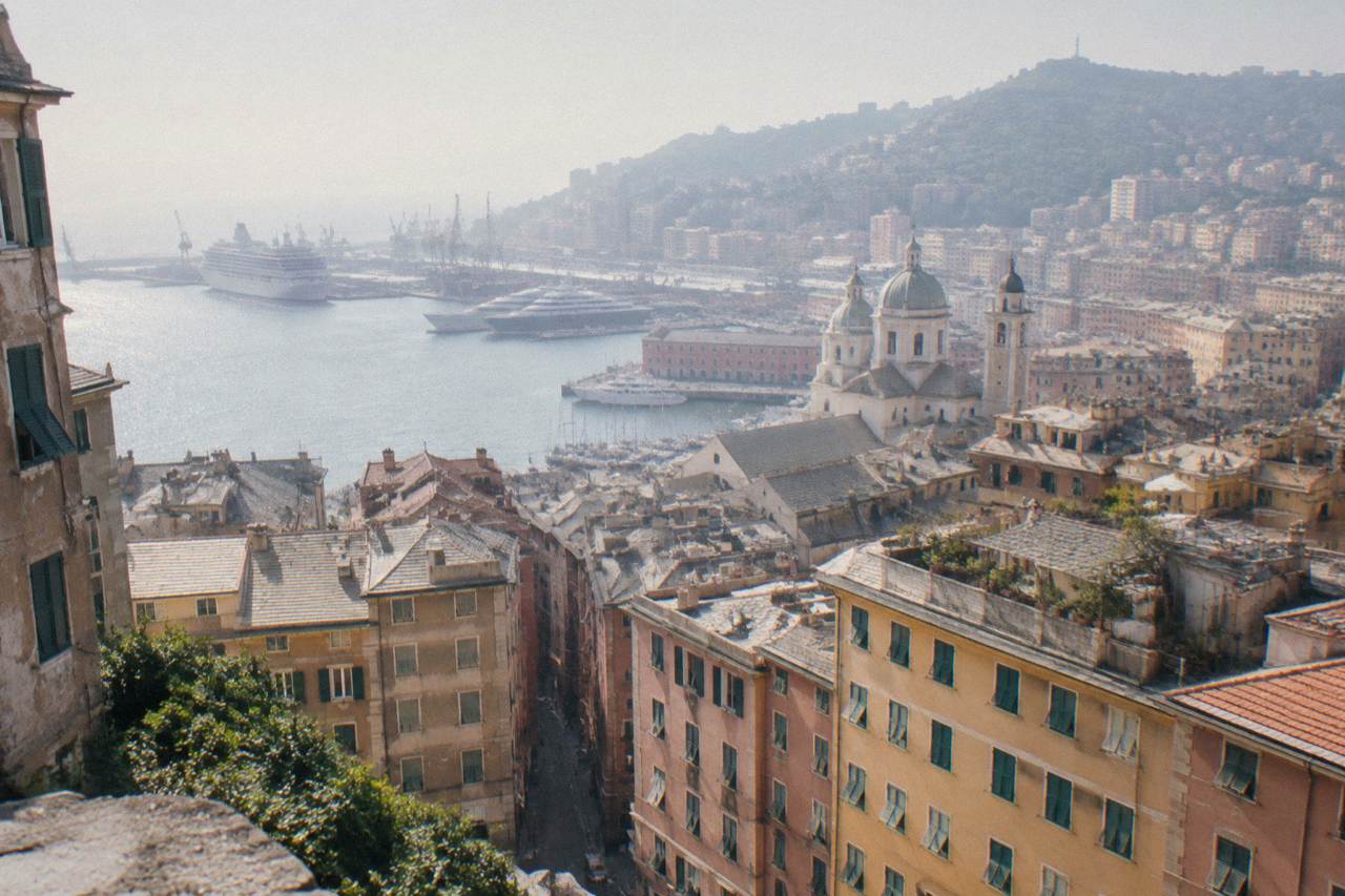 The harbour of Genoa with ships moored along the waterfront and hills rising behind the city