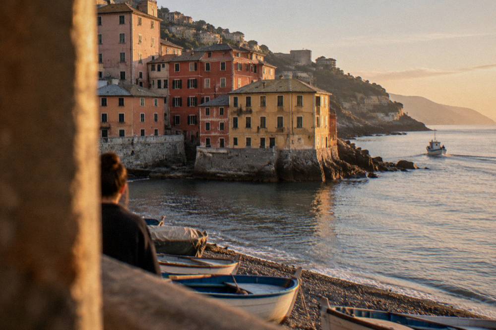 A small boat rounding the headland past the coloured waterfront of Boccadasse
