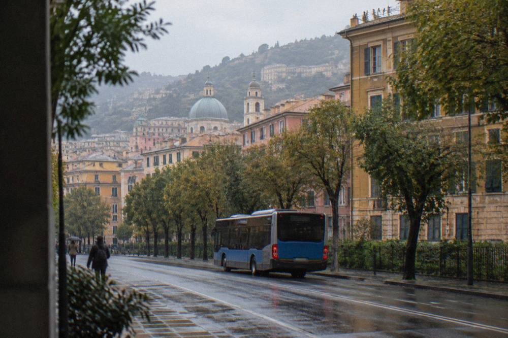 A city bus moving along a tree-lined residential street in eastern Genoa