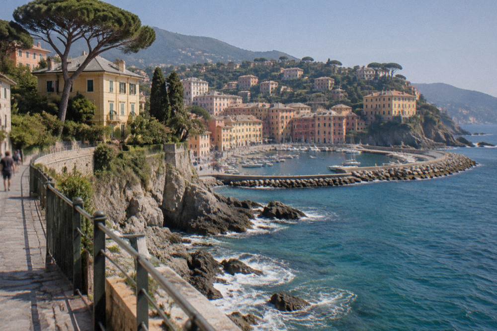 A curved stone breakwater enclosing a small harbour with moored boats and apartment buildings on the hillside behind