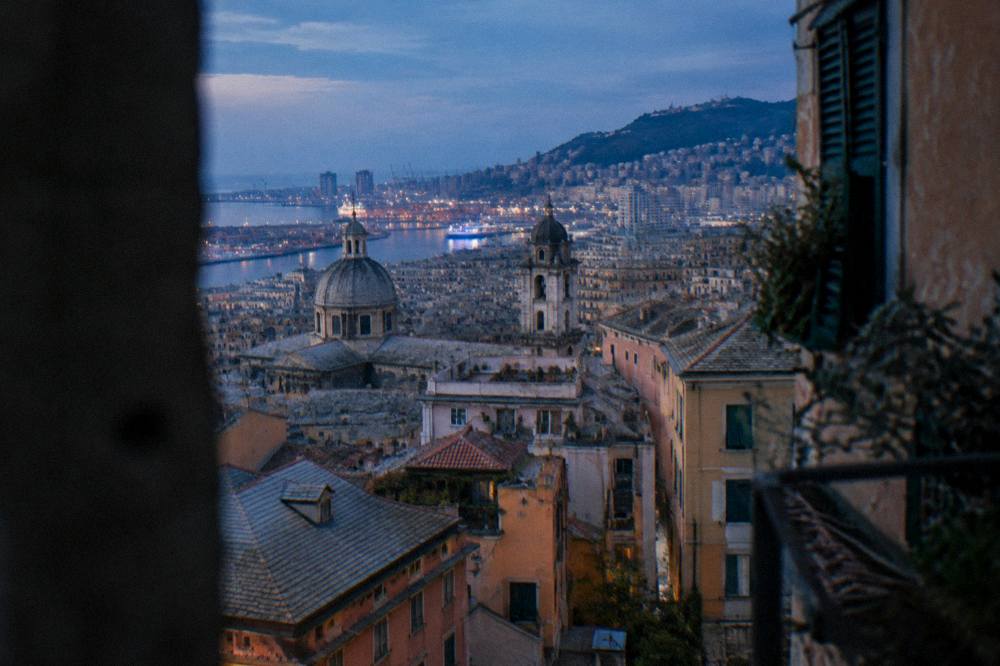Evening view over rooftops of central Genoa with the harbour lights in the distance