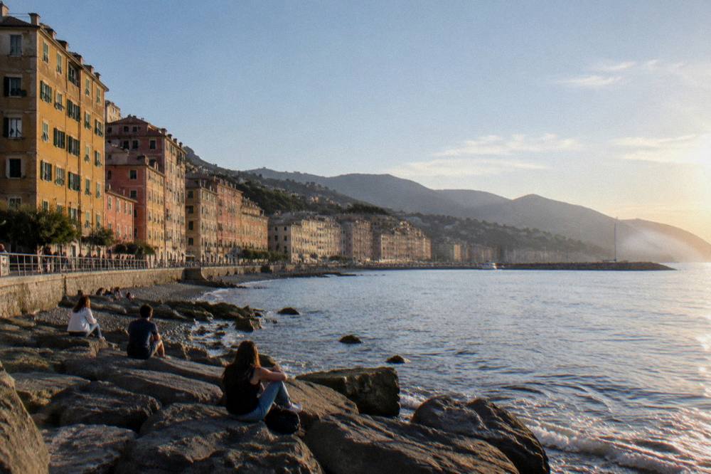 People sitting on flat rocks at the water's edge on a sunny day