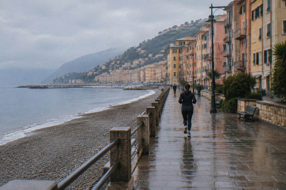 A western seaside district with a long promenade beside a pebble beach, tall faded pastel apartment blocks and calm sea