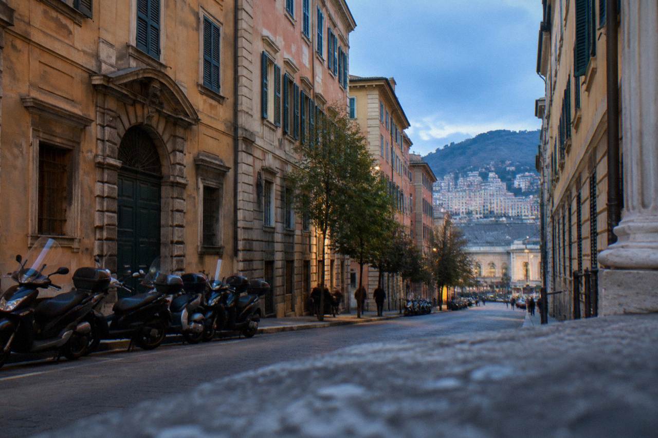 A city street with parked scooters and tall painted buildings rising up a hillside