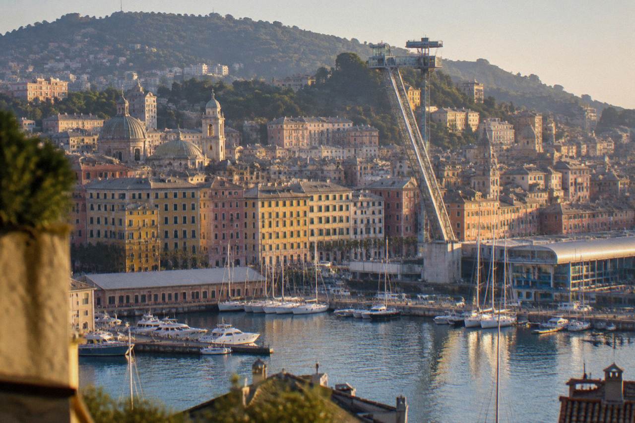 A slender crane-like panoramic lift structure rising over the old harbour of Genoa