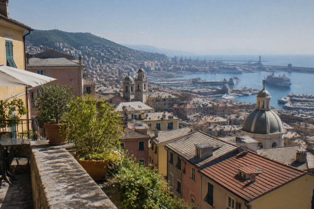 A terrace overlooking red rooftops and a harbour in Genoa from the hills above the city