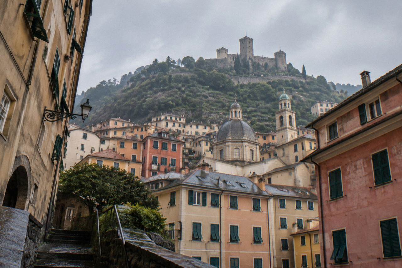 A hilltop castle with towers and terraced gardens overlooking the rooftops of Genoa and the Ligurian Sea