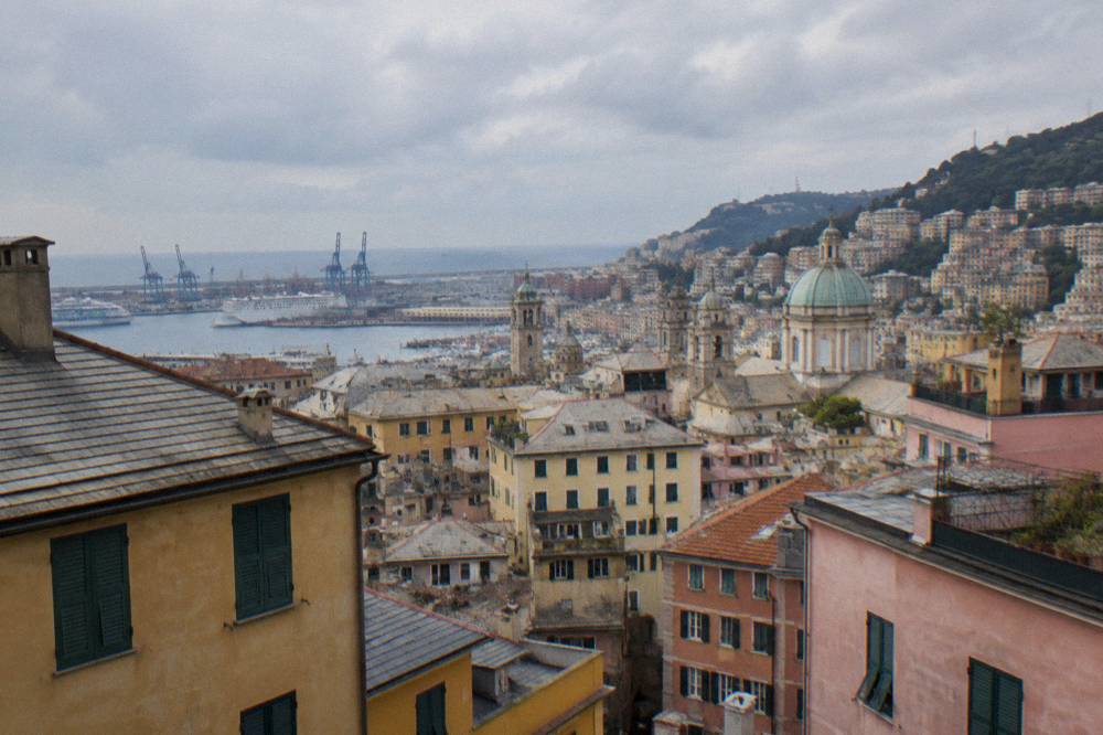 The Genoa skyline seen from a high terrace with rooftops descending toward the harbour