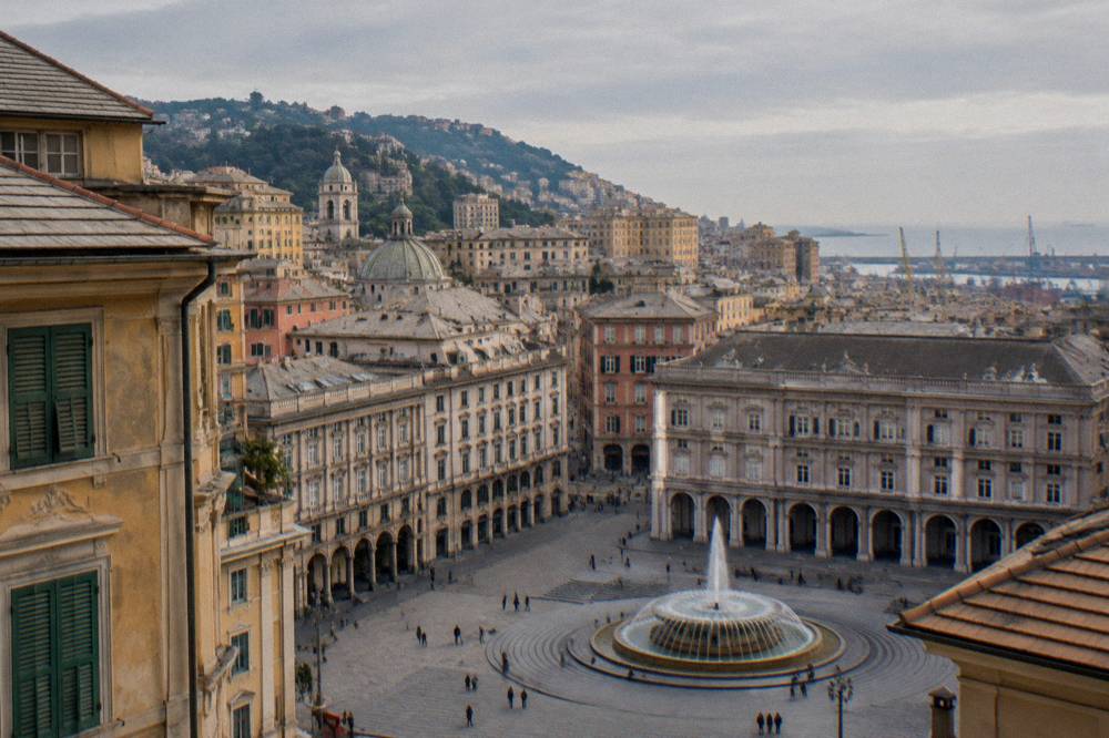 Wide city square with a large fountain and ornate buildings in Genoa