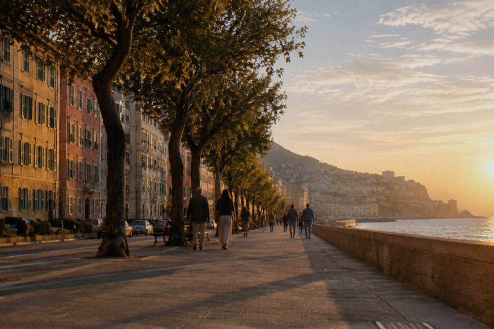 People strolling under trees along Corso Italia with the sea on one side and tall early twentieth-century apartment blocks on the other