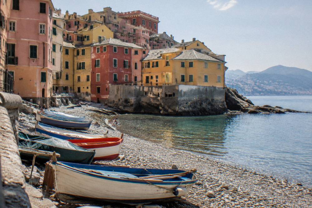 Colourful houses of Boccadasse around a small pebble beach with fishing boats pulled up on the shore