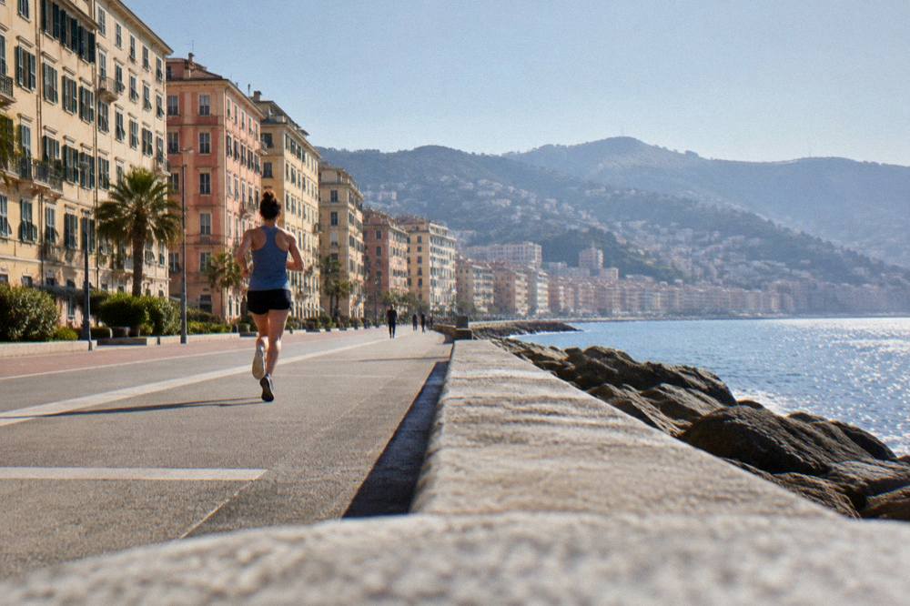 A runner on the flat seafront promenade in morning light with the Ligurian Sea beside the path
