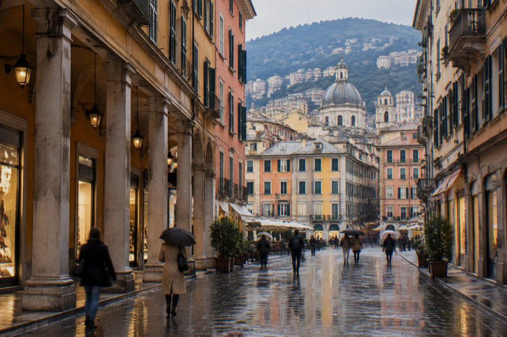 Rain-slicked shopping street with porticoes and lit shopfronts in Genoa