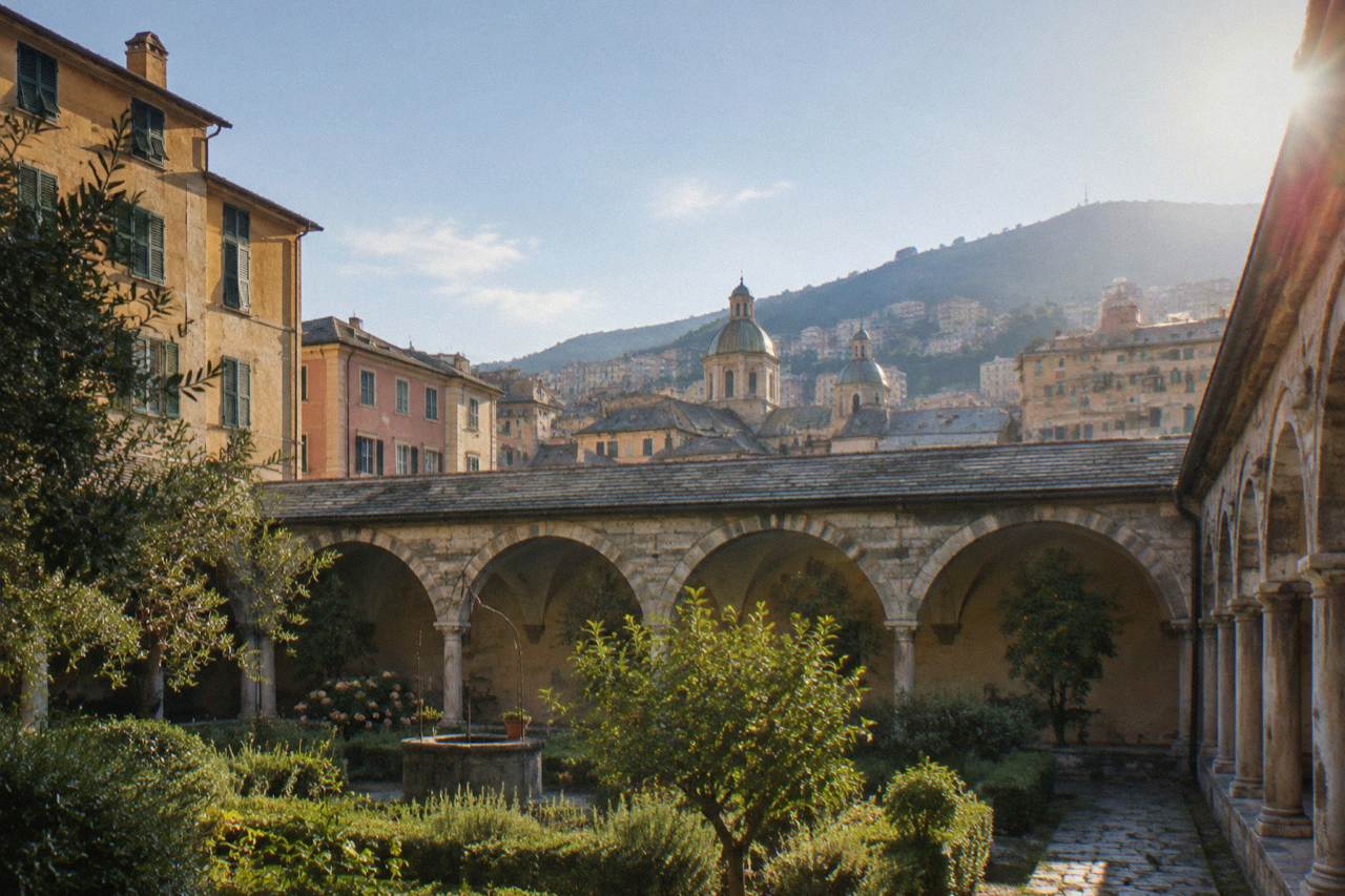 Stone arches of a cloister in Genoa enclosing a quiet garden courtyard