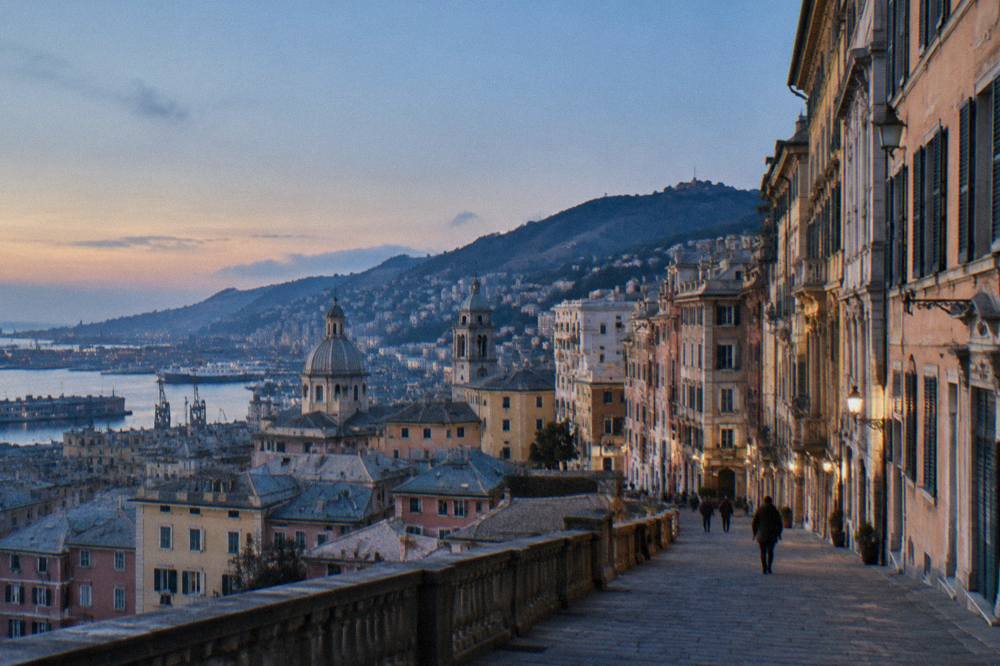 A long city street of ornate palace facades stepping up a hillside in Genoa