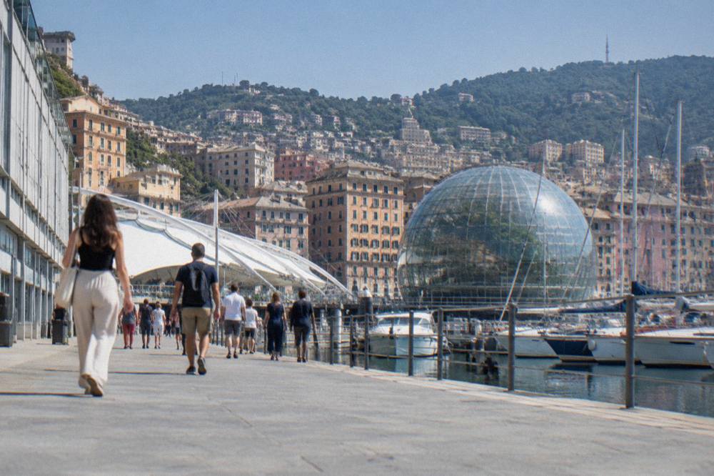 Visitors walking along the Porto Antico promenade in Genoa with the glass Biosfera sphere in the background