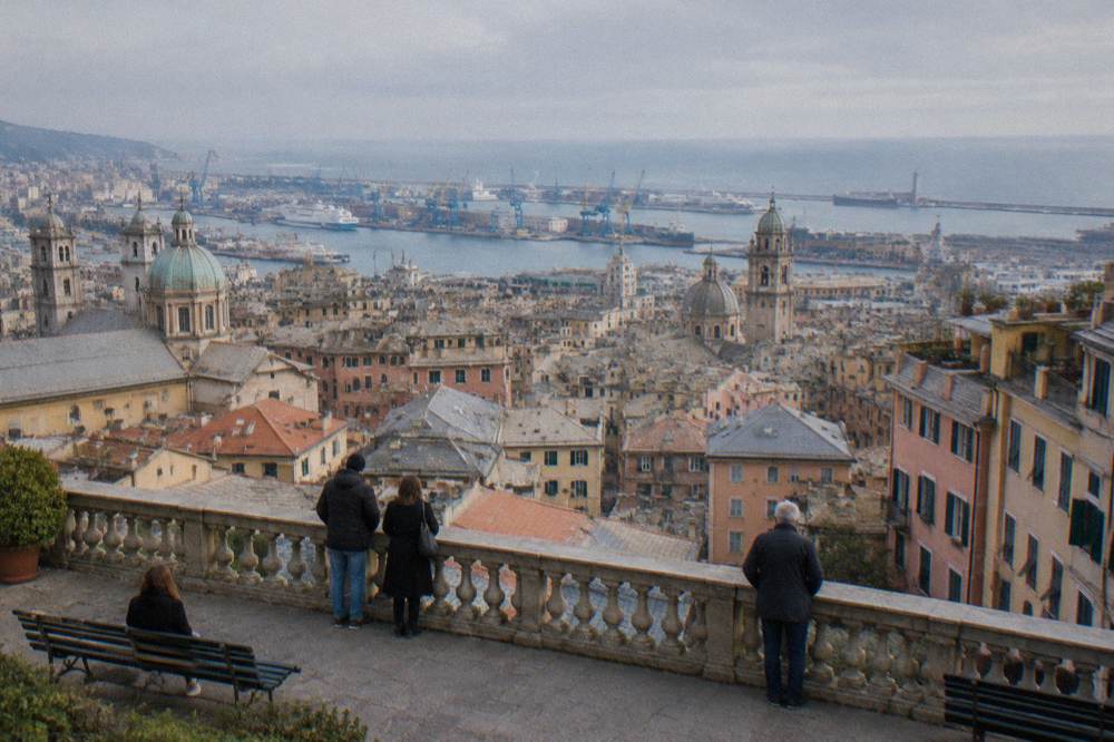 People at a stone railing of a panoramic terrace looking over a port city