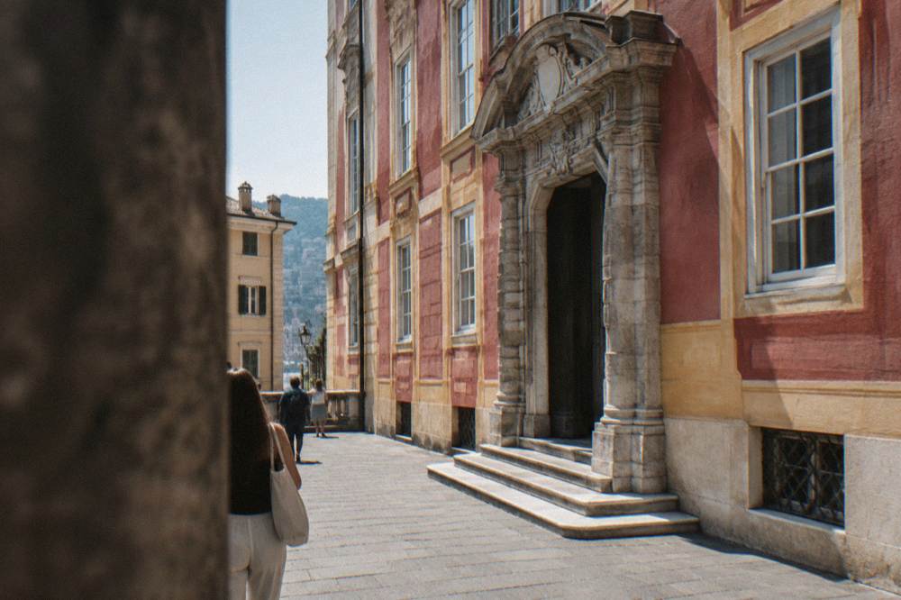 A grand sixteenth-century palace with a deep rose and ochre stucco front, white-framed windows and a heavy carved stone portal on a narrow pedestrian street