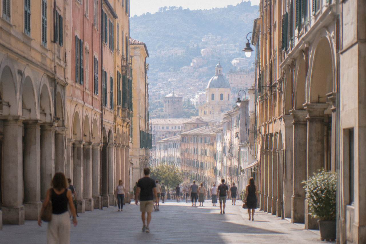 An arcaded shopping street in Genoa with tall buildings on both sides and people walking along the pavements