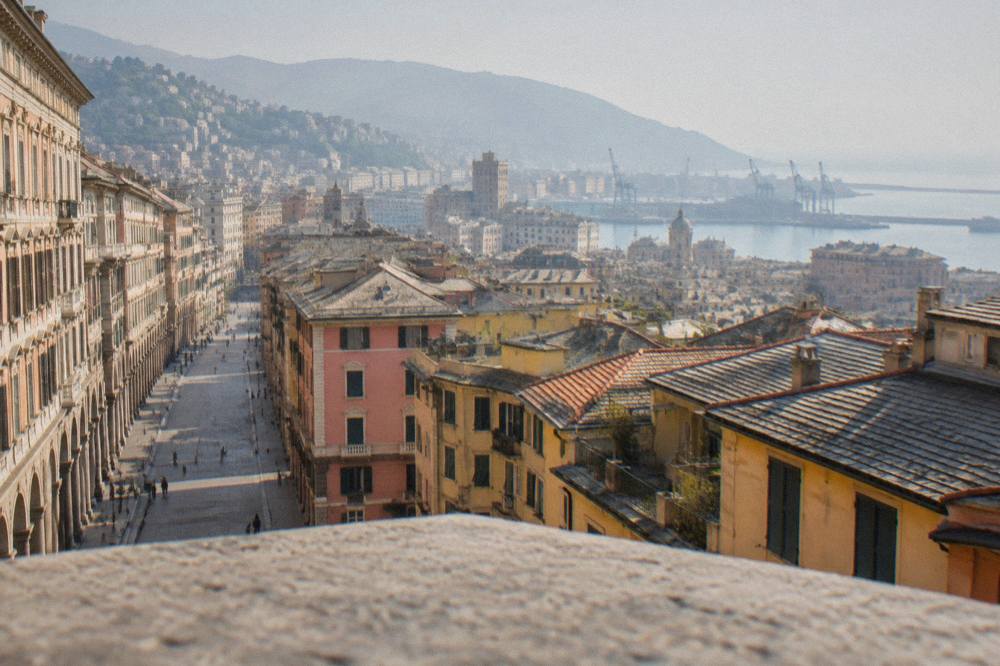 A view across rooftops toward the sea and hills from a high terrace in Genoa