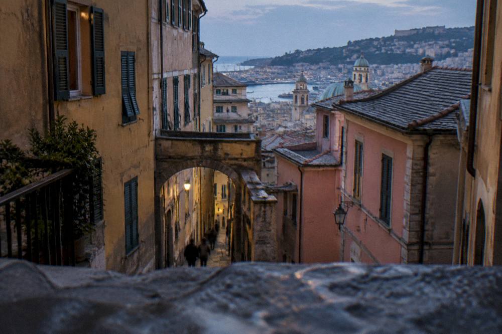 A narrow medieval lane in Genoa with tall painted buildings and stone arches