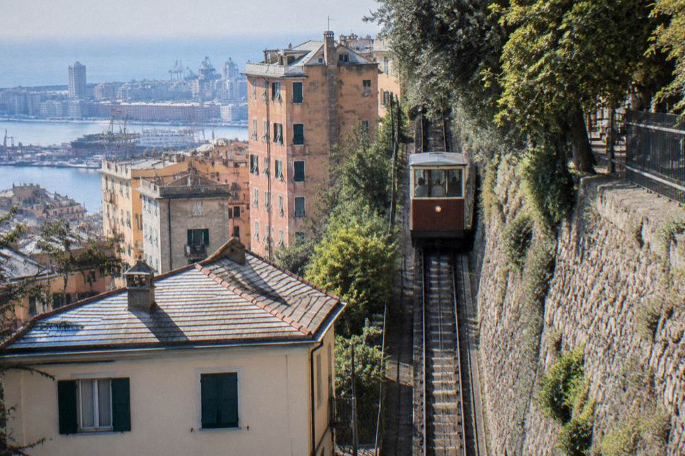 A small old cable railway car climbing a steep cutting between stone retaining walls and trees on a narrow track