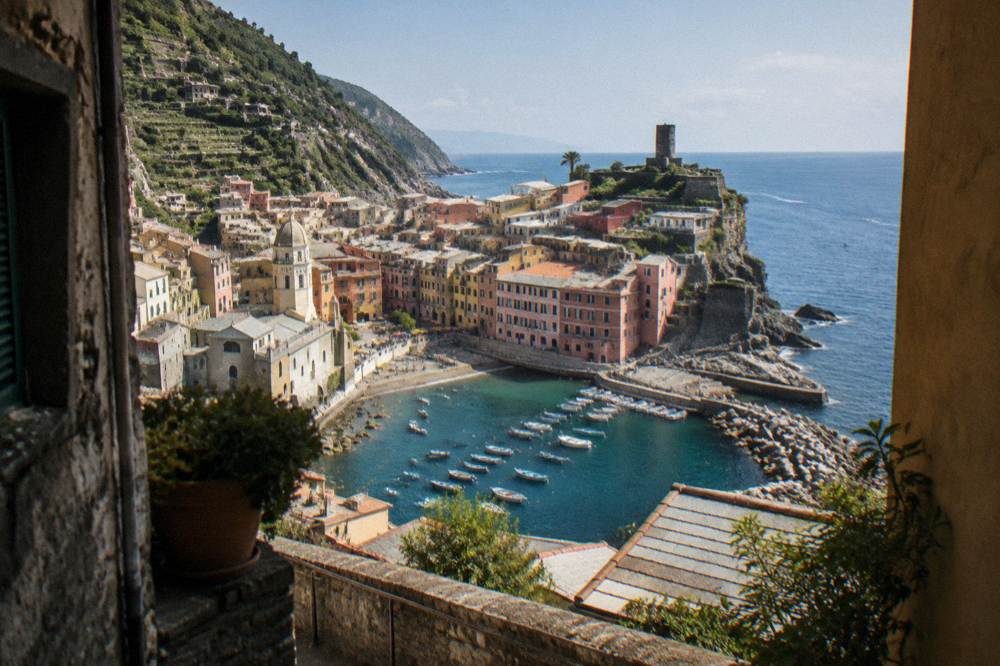 A steep fishing village of pastel houses stacked down a cliff to a tiny harbour with terraced vines high on the slopes above a dark blue sea