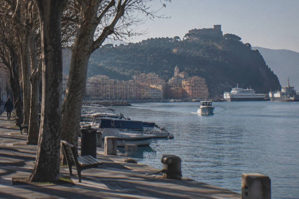 A small boat approaching a pastel-coloured harbour village at the foot of wooded cliffs