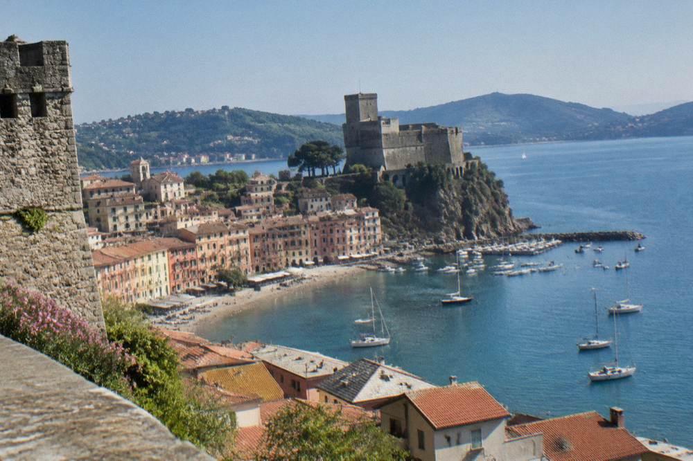 A stone castle keep above rooftops looking out over a wide blue bay