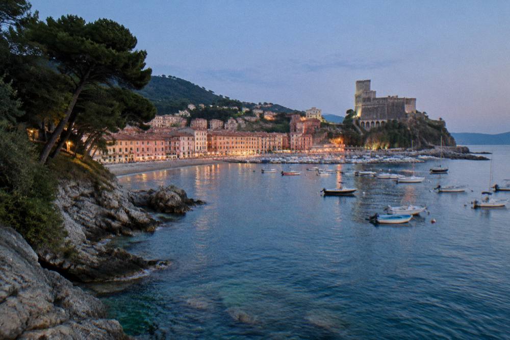 Wooded headland above clear water with small boats near a rocky shore