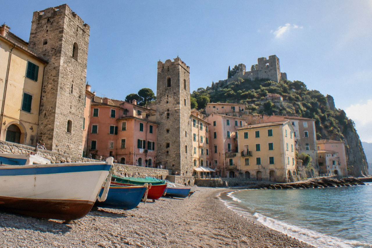 A small Ligurian seaside town with stone towers above a curved sandy beach and colourful boats