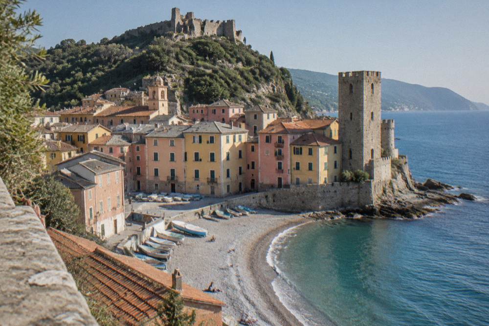 A stone watchtower standing above pastel houses near the water's edge