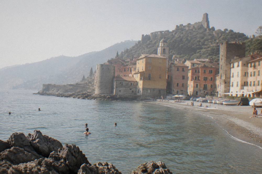 People swimming near a rocky shoreline beside a small sandy beach
