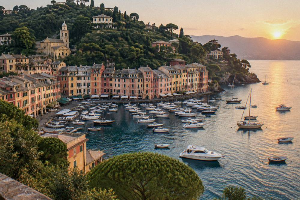 Boats moored in a small harbour at sunset with hills behind