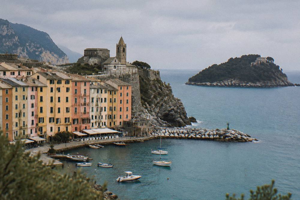 Turquoise water between a mainland cliff and a wooded island with a small stone building