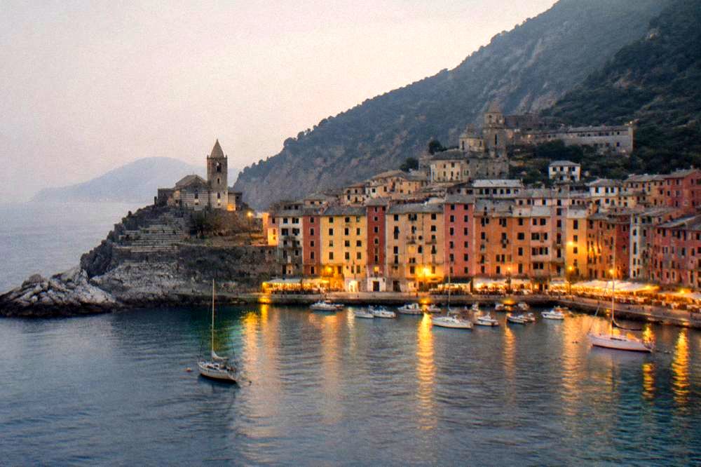 Evening view of a lit harbour village from the water with dark hills behind